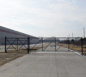 A black chain link cantilever gate set up on a private road near an industrial building