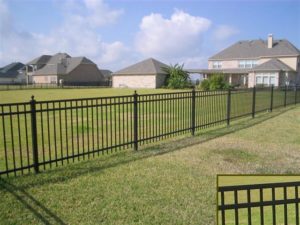 An ornamental iron flat top fence stretches across a length of a backyard. A closeup is featured of the spear-free flat top of the fence