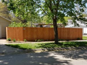 A stained cedar-tone fir fence with an American Fence logo plate in the upper left corner