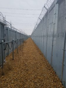 Between two sections of the high security fence with outer side being much taller than the inner side