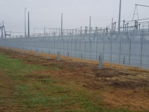 A length of high security fence encompassing large industrial features 