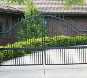 An over arch swing gate placed in front of a curved driveway lined with bright green bushes