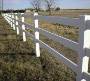 A white vinyl ranch rail fence stretching across a field slowly browning as it transitions into autumn
