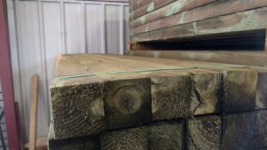 A neat stack of square green treated posts in a warehouse. The wood is slightly tinged green