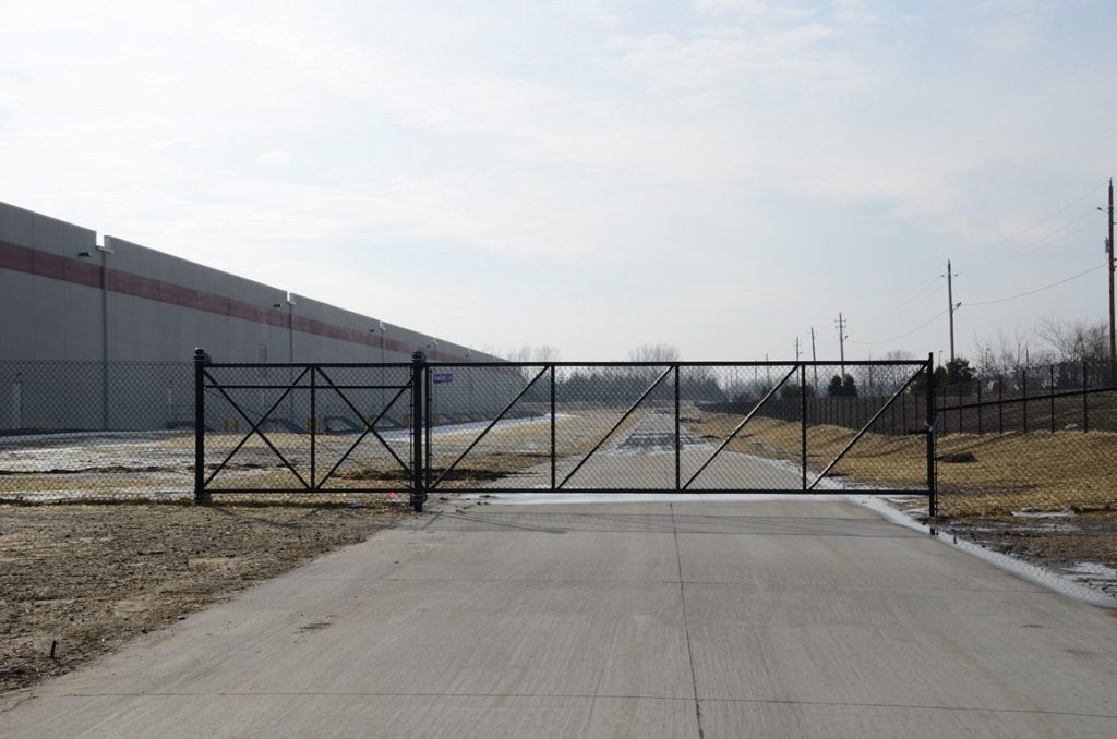 Black chain link sliding cantilever gate in front of a warehouse facility