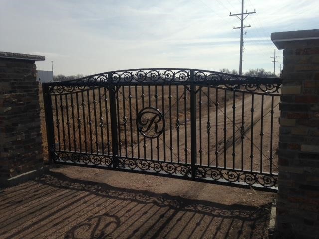 Decorative cantilever gate installed in front of a driveway with intricate scroll work and a custom "R" in the middle